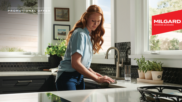 Woman cleaning kitchen counter by window.