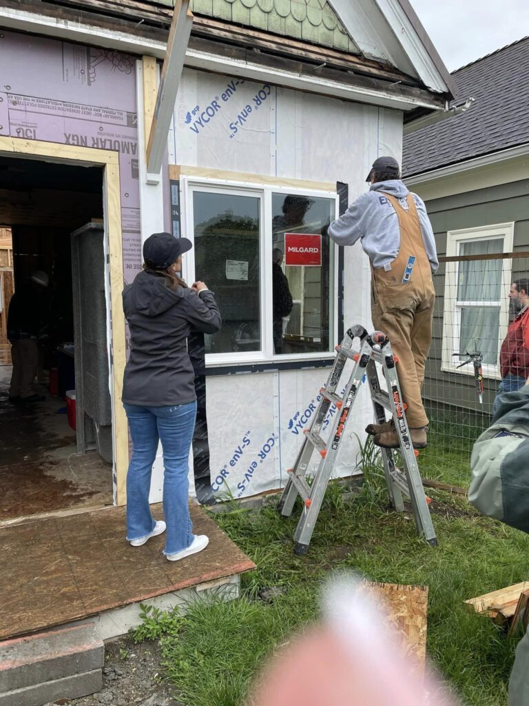 Workers installing new window on house exterior.