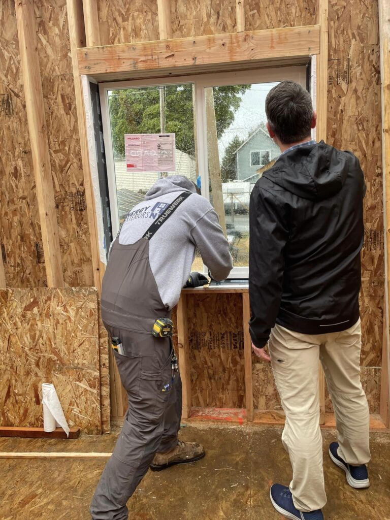 Two people installing a window in a wooden frame.