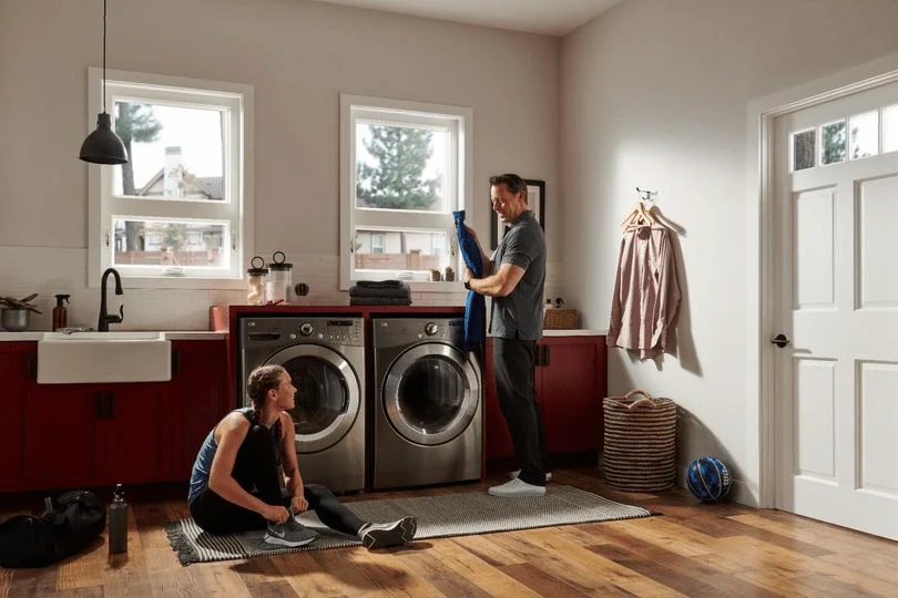 Men in laundry room, one folding towel, one stretching