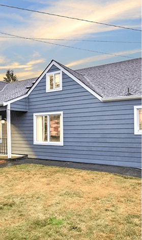 Blue house with gray roof and green lawn at dusk